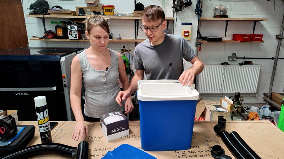 All the parts laid out on a workbench before assembly — the cool box, coiled aluminium ducting, extractor fan and expanding foam tin 