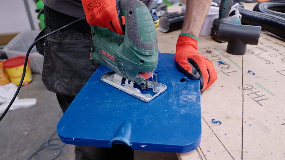 Jigsaw cutting a circular hole through the plastic lid of the cool box