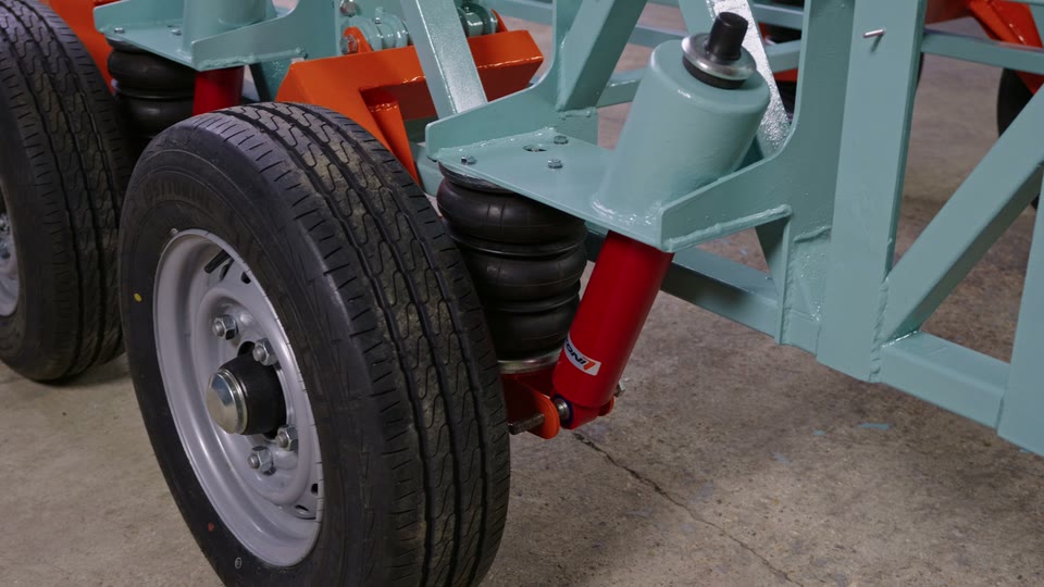 Close-up of a DIY tiny house trailer's independent suspension: orange swing arm, black air bag and red shock absorber